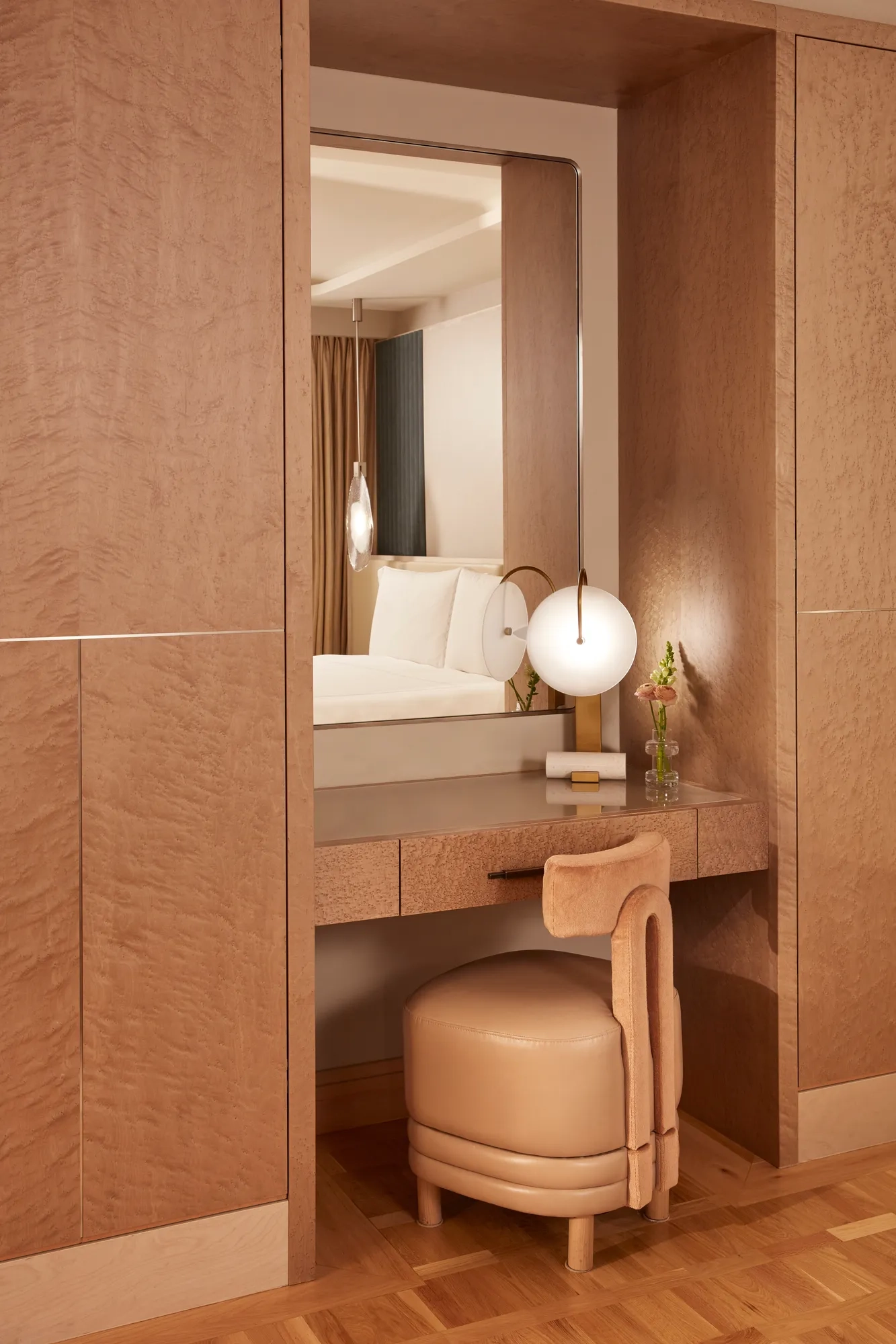 Elegant vanity area with a soft leather stool, large mirror, and spherical table lamp, finished in warm wood tones and soft lighting.