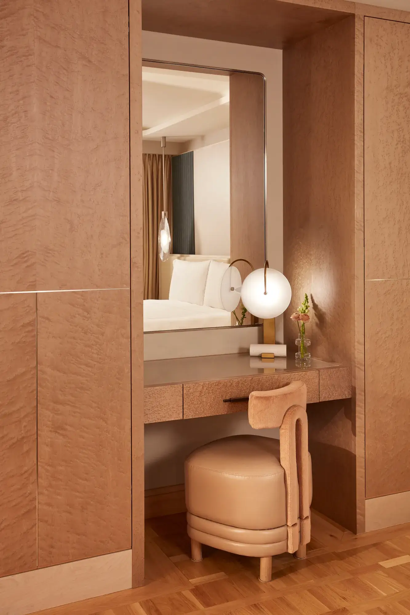 Elegant vanity area with a soft leather stool, large mirror, and spherical table lamp, finished in warm wood tones and soft lighting.