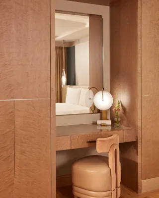 Elegant vanity area with a soft leather stool, large mirror, and spherical table lamp, finished in warm wood tones and soft lighting.