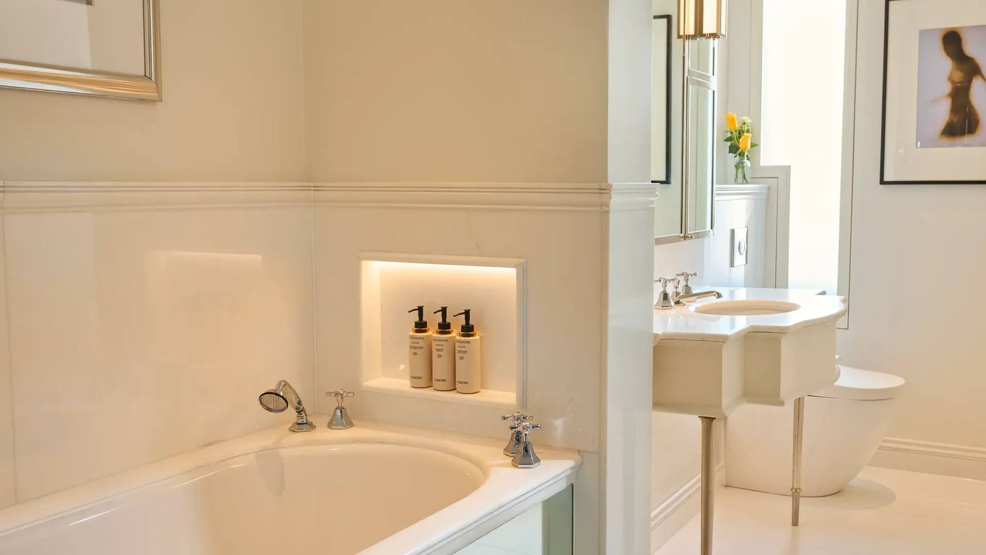 Bright marble bathroom with bathtub, vanity sink, and toilet in adjoining alcove.