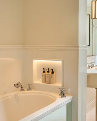 Bright marble bathroom with bathtub, vanity sink, and toilet in adjoining alcove.