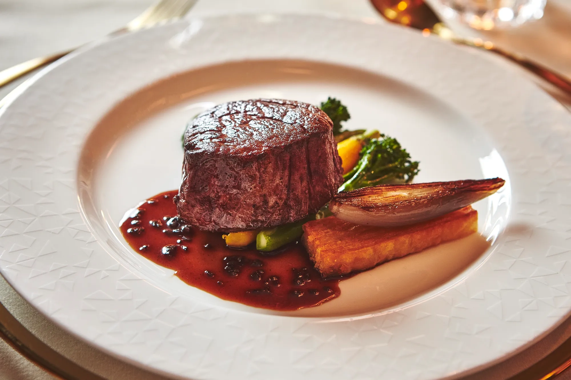 Plated beef fillet with red wine sauce, roasted vegetables and potato on a white fine-dining plate.