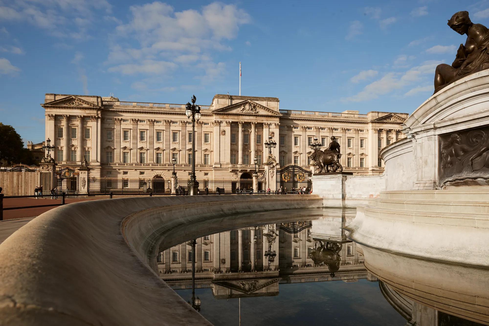 Buckingham Palace and the Victoria Memorial reflected in the fountain under a clear blue sky.