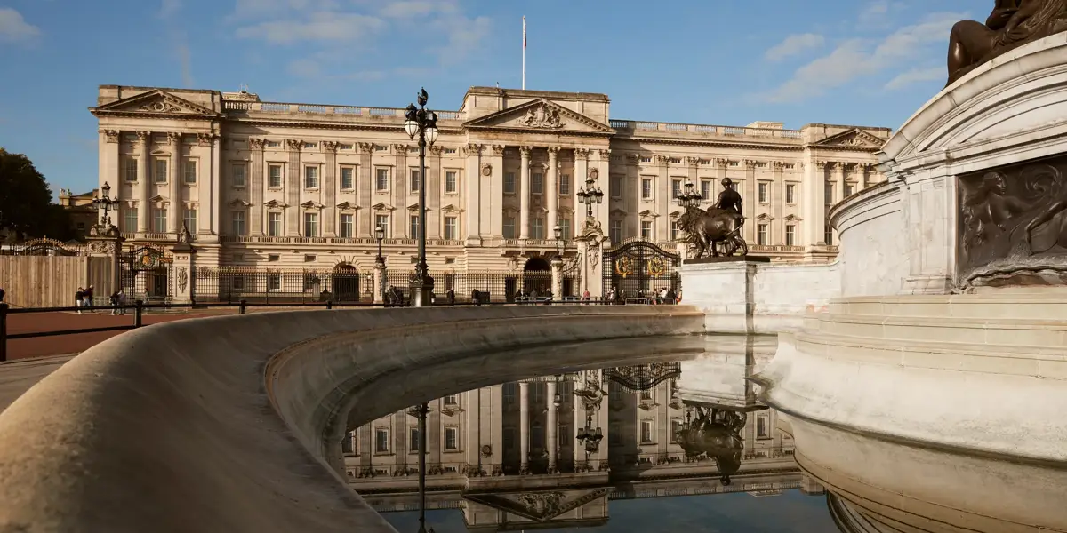 Buckingham Palace and the Victoria Memorial reflected in the fountain under a clear blue sky.
