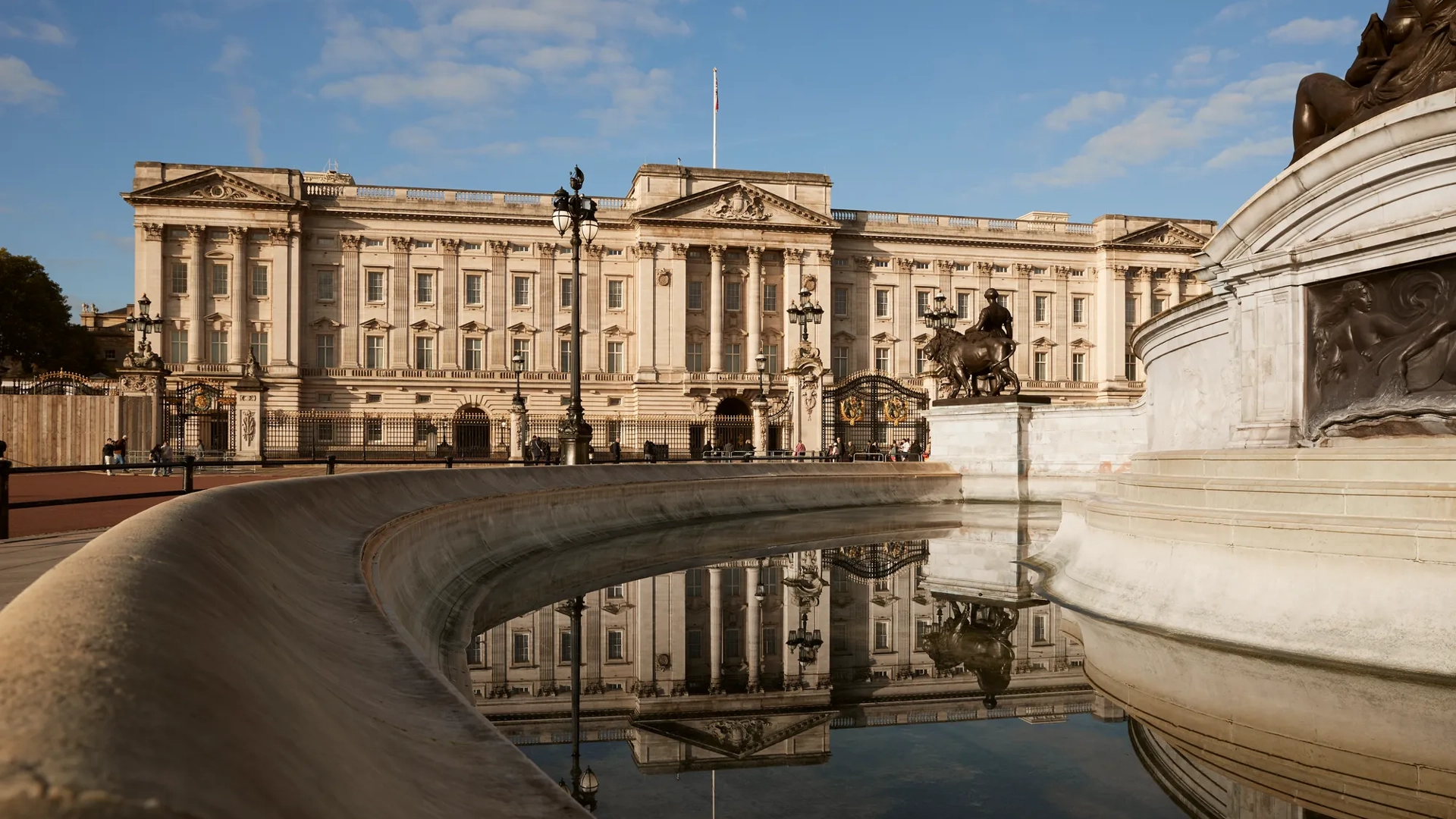 Buckingham Palace and the Victoria Memorial reflected in the fountain under a clear blue sky.