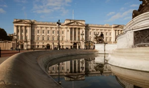 Buckingham Palace and the Victoria Memorial reflected in the fountain under a clear blue sky.