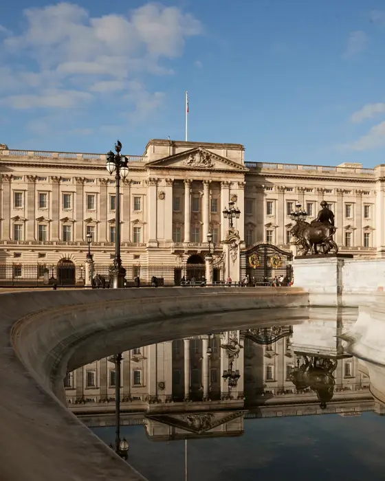 Buckingham Palace and the Victoria Memorial reflected in the fountain under a clear blue sky.