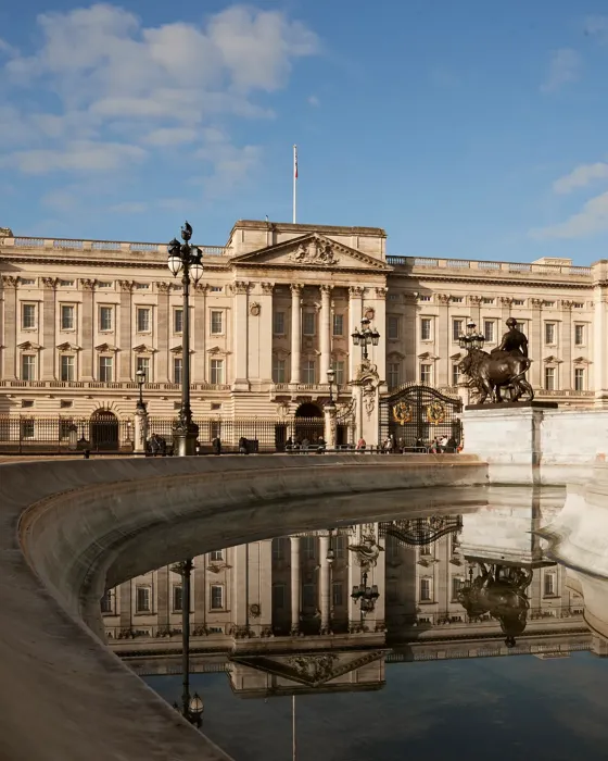 Buckingham Palace and the Victoria Memorial reflected in the fountain under a clear blue sky.