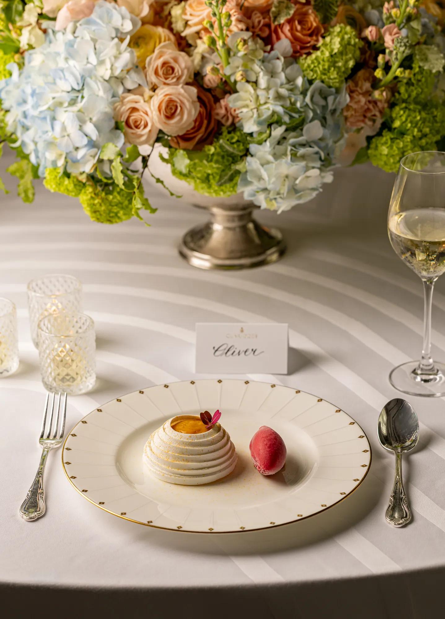 Elegant dessert place setting with plated pastry, sorbet, floral centrepiece, and glass of sparkling wine.
