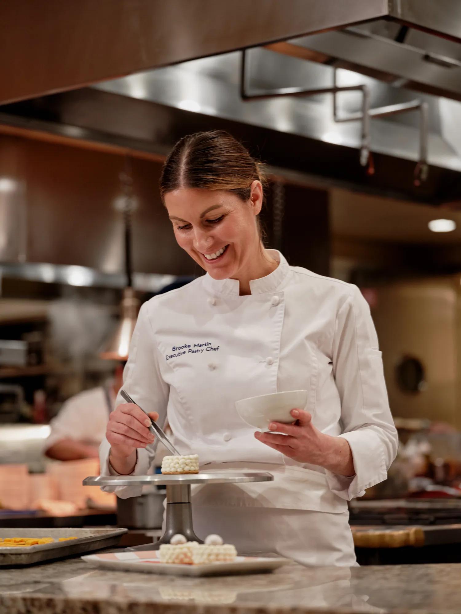 Executive Pastry Chef Brooke Martin carefully plates a petite, pearl‑topped dessert in the hotel kitchen.