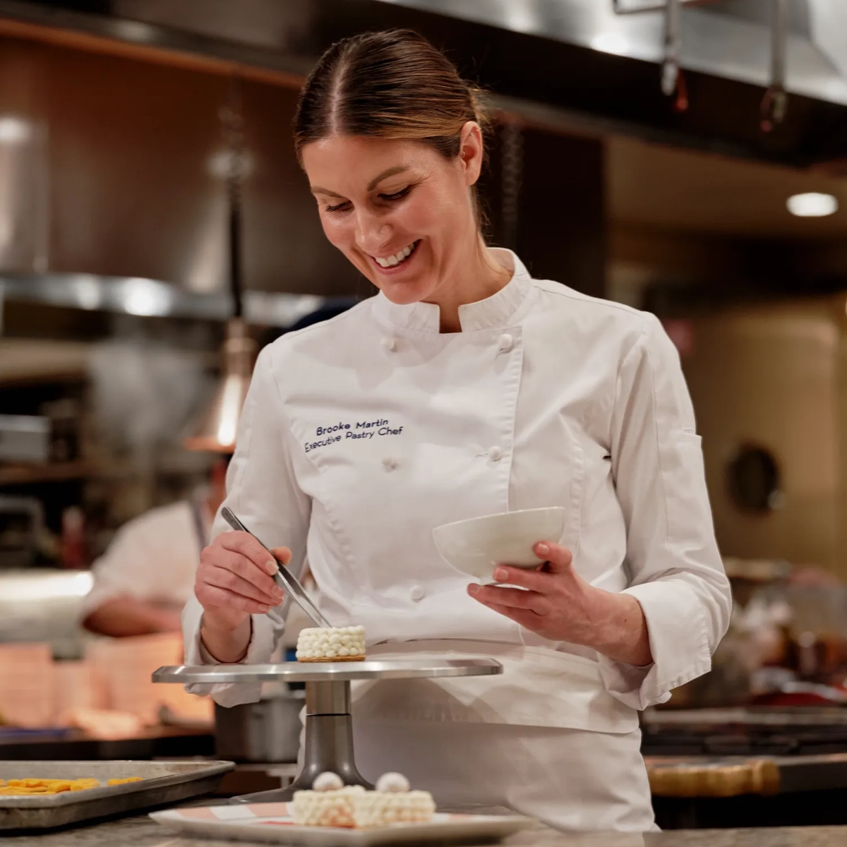Executive Pastry Chef Brooke Martin carefully plates a petite, pearl‑topped dessert in the hotel kitchen.