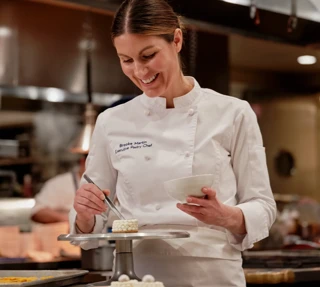 Executive Pastry Chef Brooke Martin carefully plates a petite, pearl‑topped dessert in the hotel kitchen.