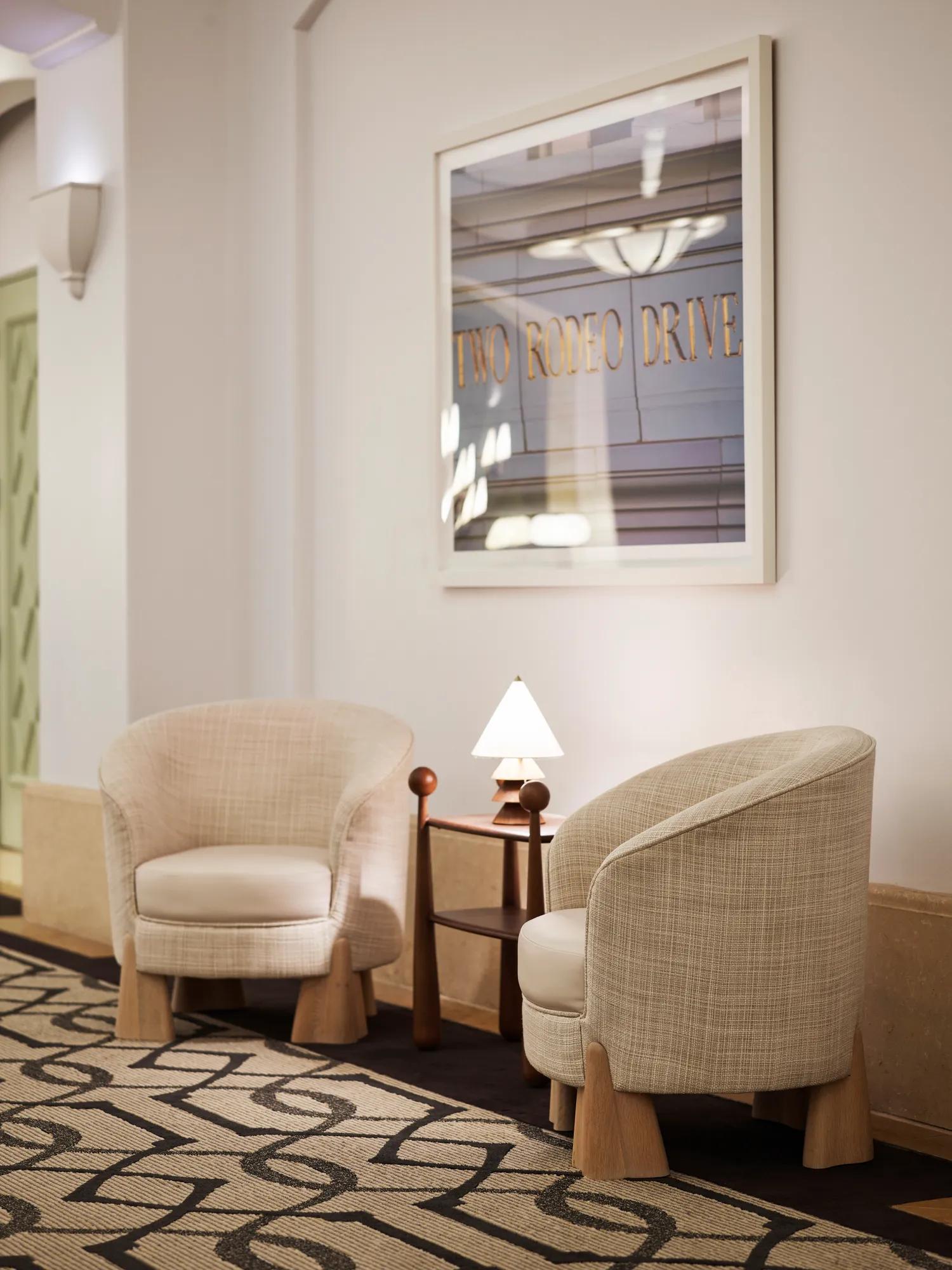 Ballroom foyer lounge area with two upholstered chairs, small lamp table, and framed “Two Rodeo Drive” artwork.