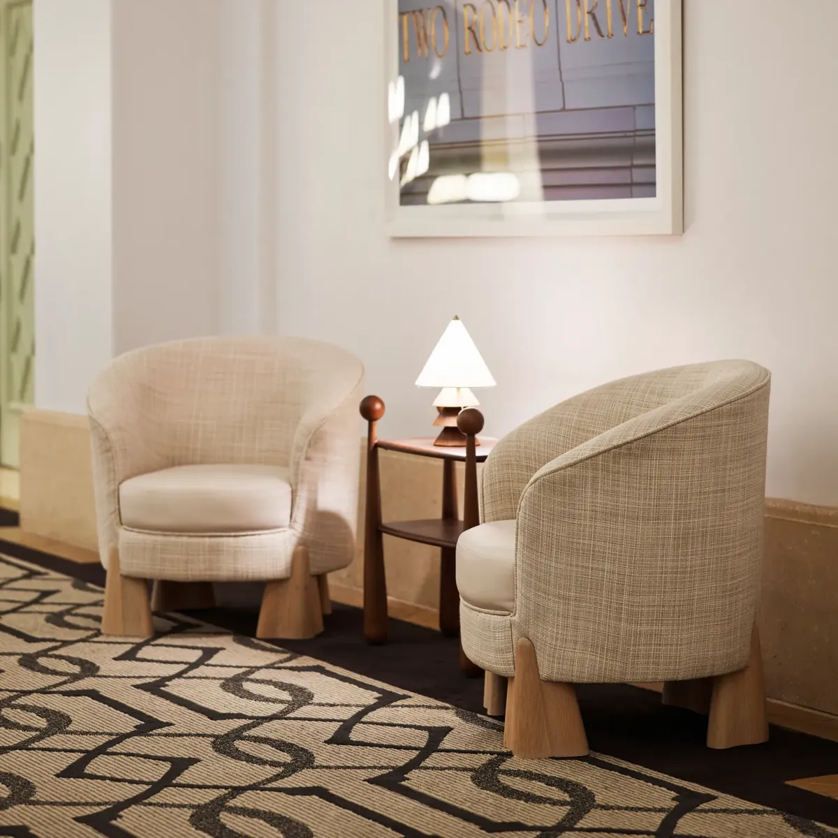 Ballroom foyer lounge area with two upholstered chairs, small lamp table, and framed “Two Rodeo Drive” artwork.