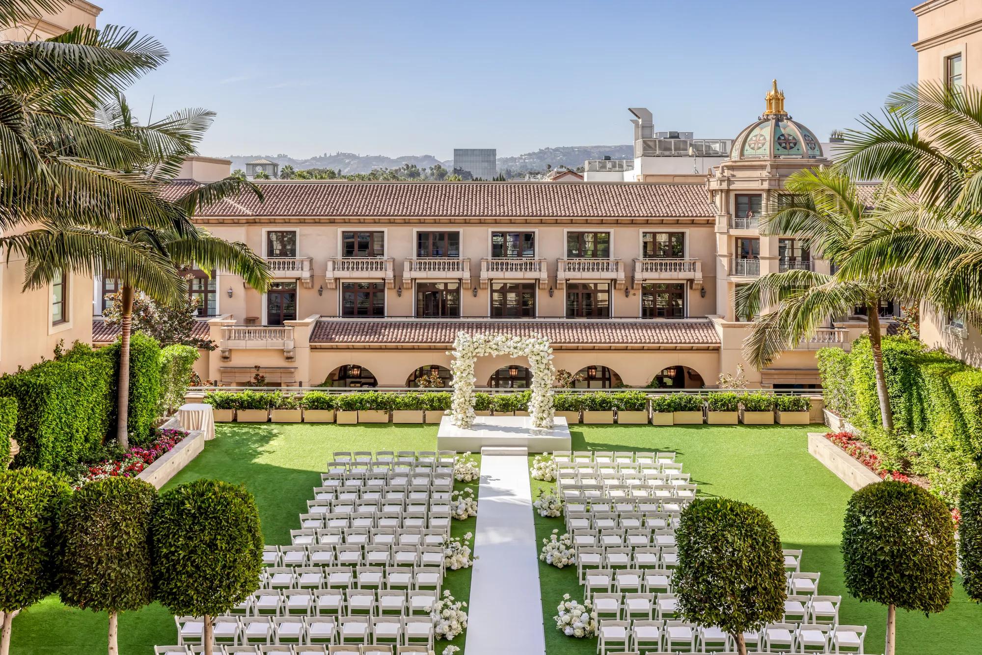 Garden Terrace wedding ceremony setup: long white aisle to a floral arch, rows of white chairs, palms and the domed rooftop beyond.