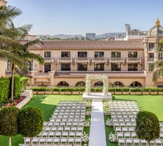 Garden Terrace wedding ceremony setup: long white aisle to a floral arch, rows of white chairs, palms and the domed rooftop beyond.