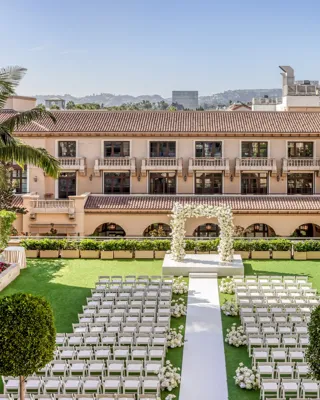 Garden Terrace wedding ceremony setup: long white aisle to a floral arch, rows of white chairs, palms and the domed rooftop beyond.
