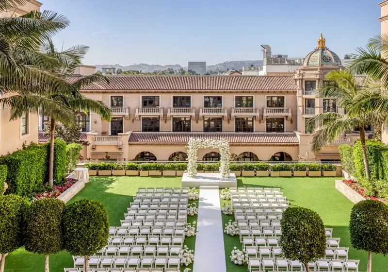 Garden Terrace wedding ceremony setup: long white aisle to a floral arch, rows of white chairs, palms and the domed rooftop beyond.