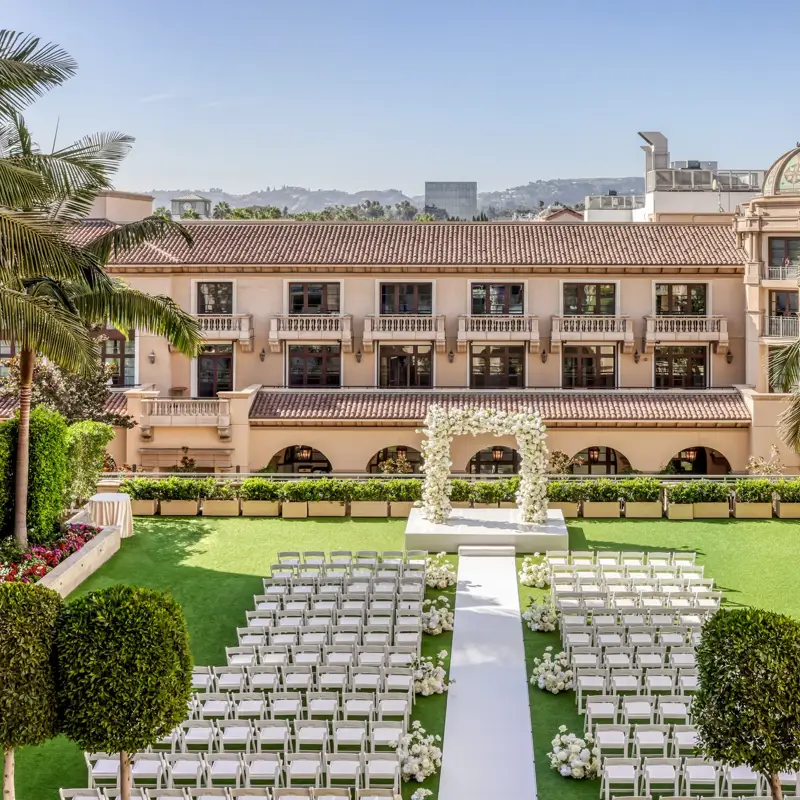 Garden Terrace wedding ceremony setup: long white aisle to a floral arch, rows of white chairs, palms and the domed rooftop beyond.