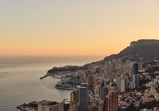 Monaco skyline at sunset with coastal high-rises, harbour, and mountains under warm golden light