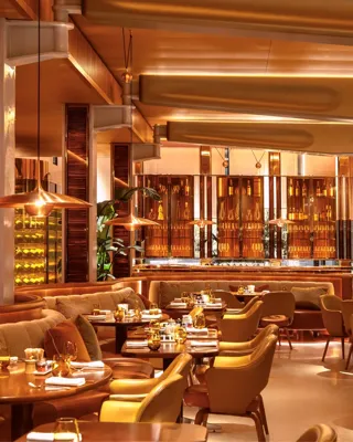Elegant restaurant interior with warm amber lighting, curved seating, and polished tables set for dining.