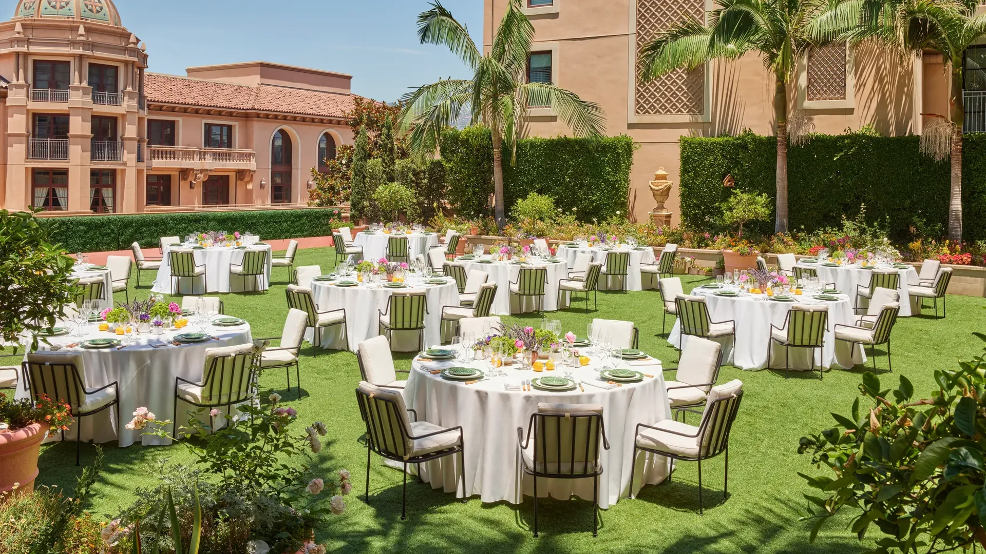 Outdoor reception on the Garden Terrace with round tables, white linens, striped cushioned chairs, colorful centerpieces, palms and domed tower.