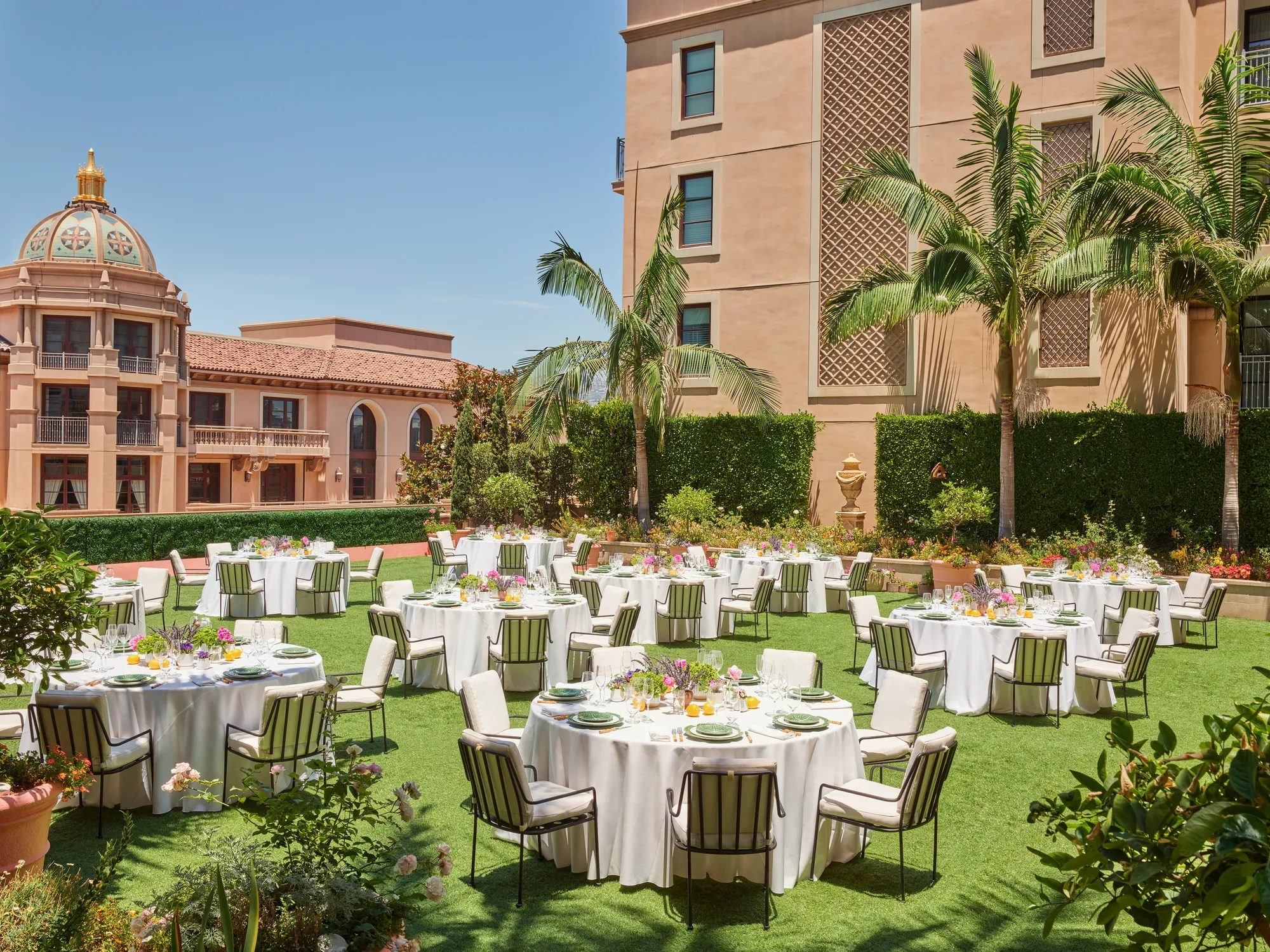 Outdoor reception on the Garden Terrace with round tables, white linens, striped cushioned chairs, colorful centerpieces, palms and domed tower.