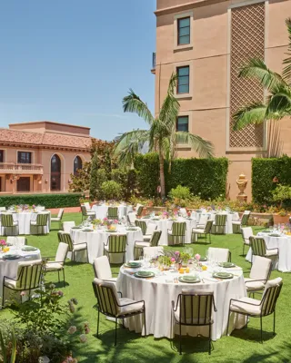 Outdoor reception on the Garden Terrace with round tables, white linens, striped cushioned chairs, colorful centerpieces, palms and domed tower.
