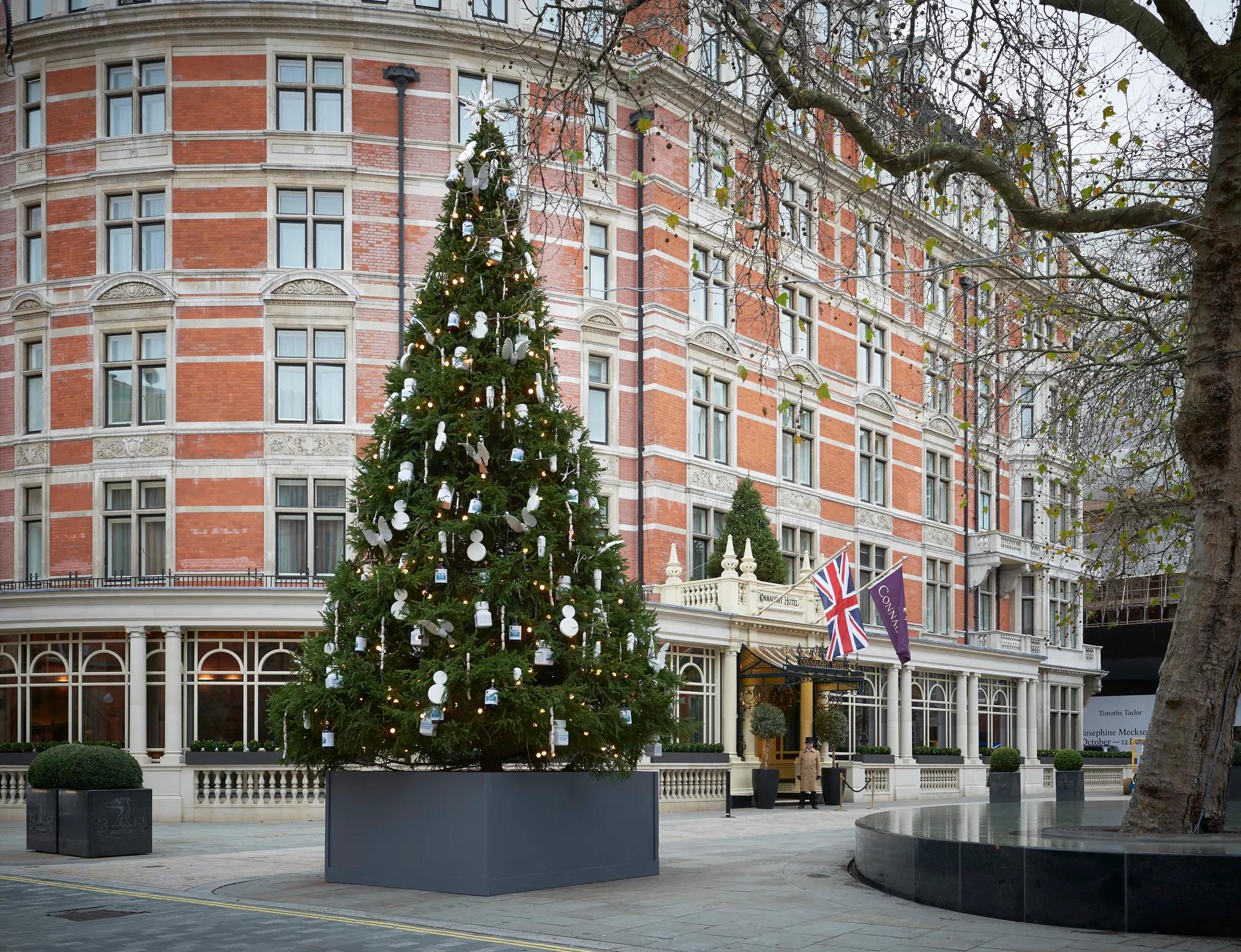 Decorated Christmas tree in planter outside grand red-brick hotel entrance on winter day.