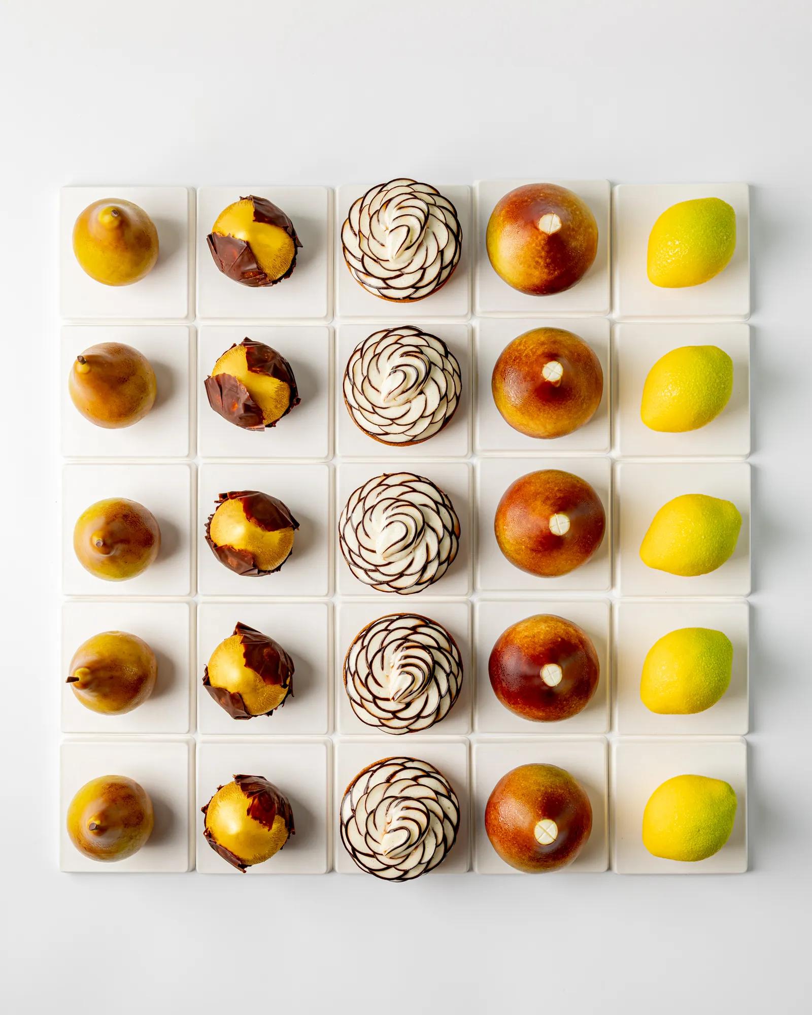 Fruit-inspired pastries and fresh fruit arranged in a geometric grid on white display blocks.