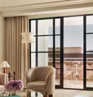 Sitting area with armchairs and a glass coffee table opening to a terrace furnished with pink chairs.