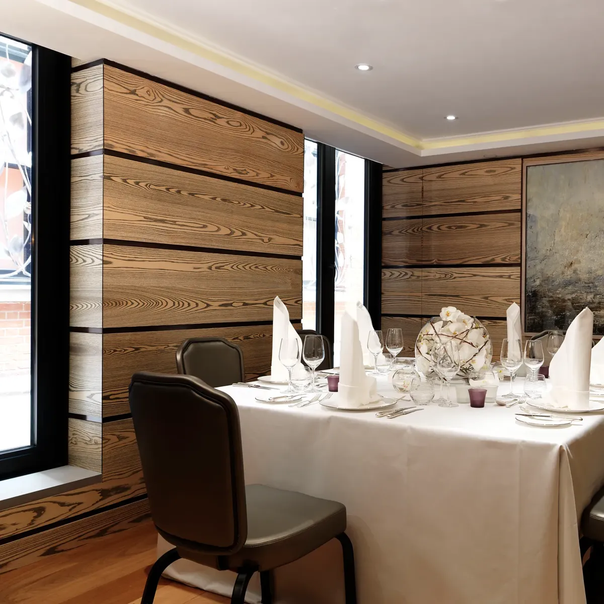 Private dining room with a square table dressed in white linens, folded napkins and glassware, surrounded by wood-panelled walls and contemporary artwork.
