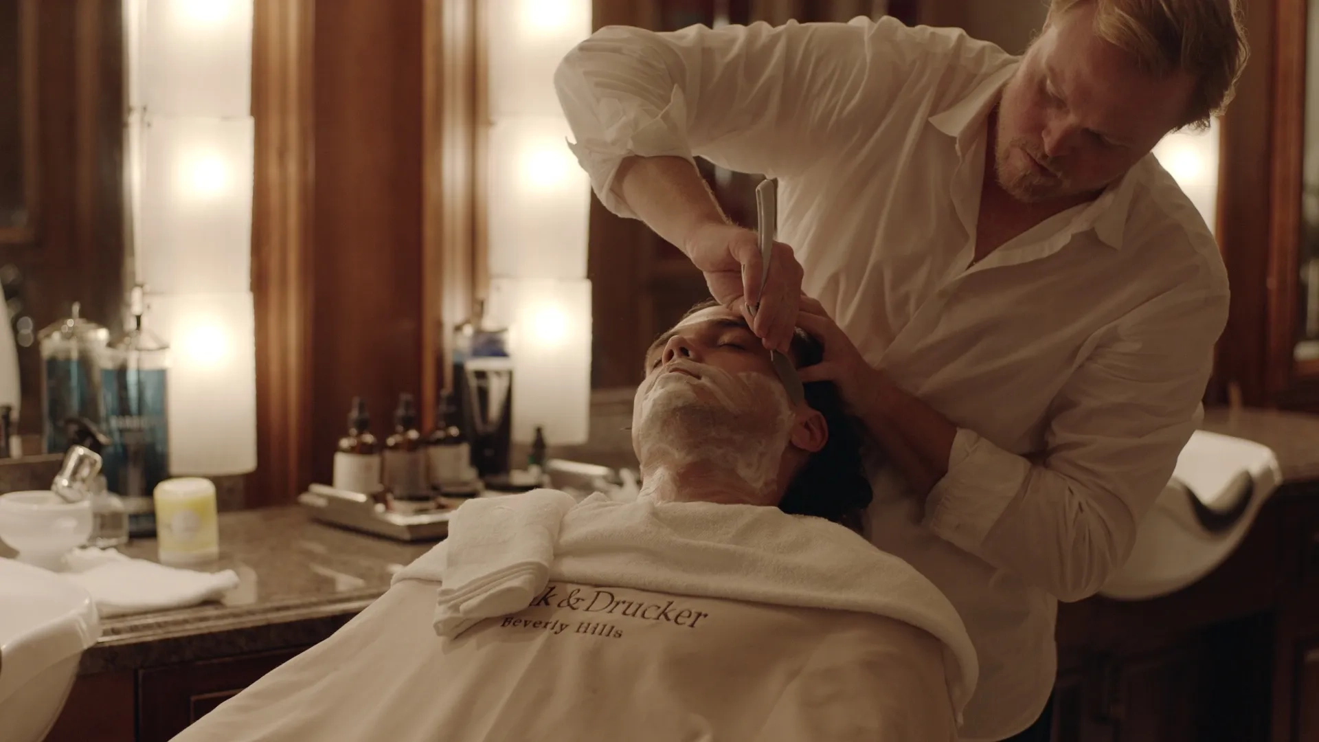Barber shaving client’s beard in vintage-style barbershop.