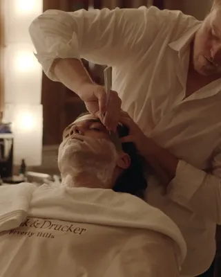 Barber shaving client’s beard in vintage-style barbershop.