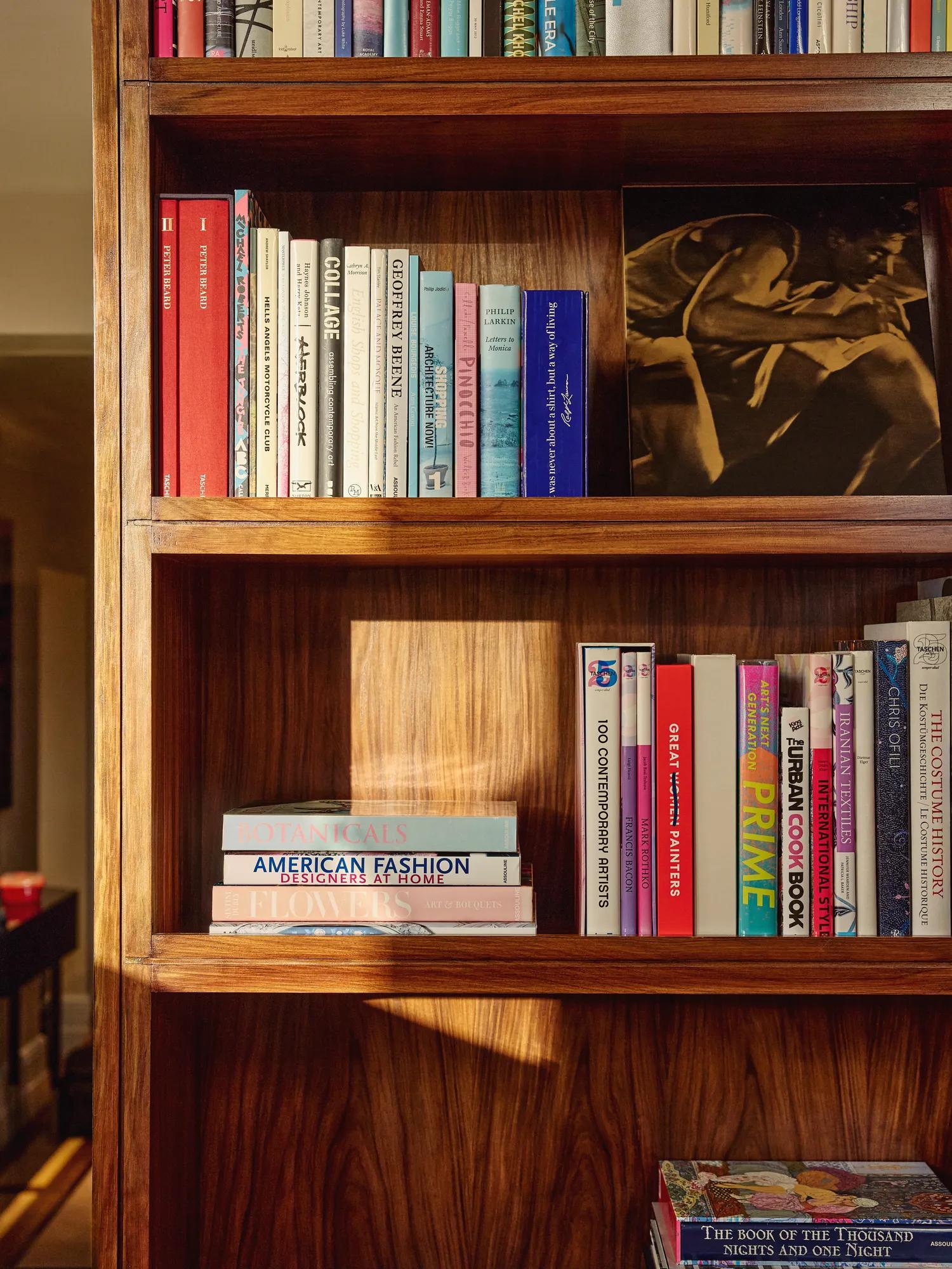Sunlit wooden bookshelf filled with colourful books and a framed black-and-white photograph.