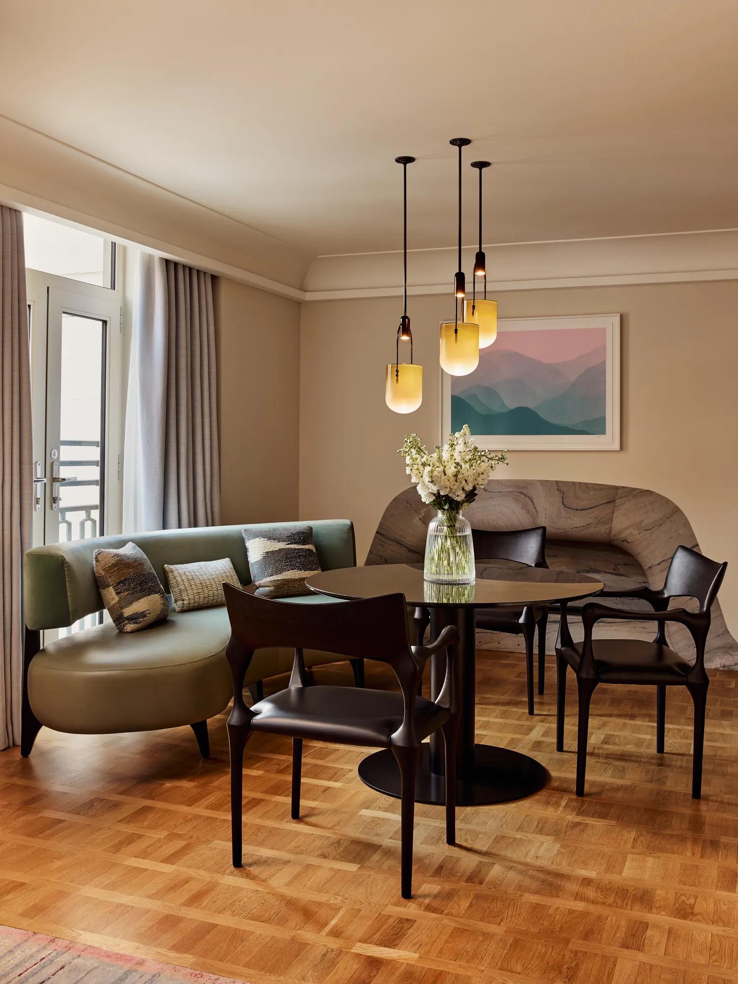 A closer view of the round dining table, green banquette seating, and decorative cushions, with sunlight streaming in through French doors.