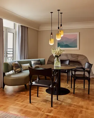 A closer view of the round dining table, green banquette seating, and decorative cushions, with sunlight streaming in through French doors.