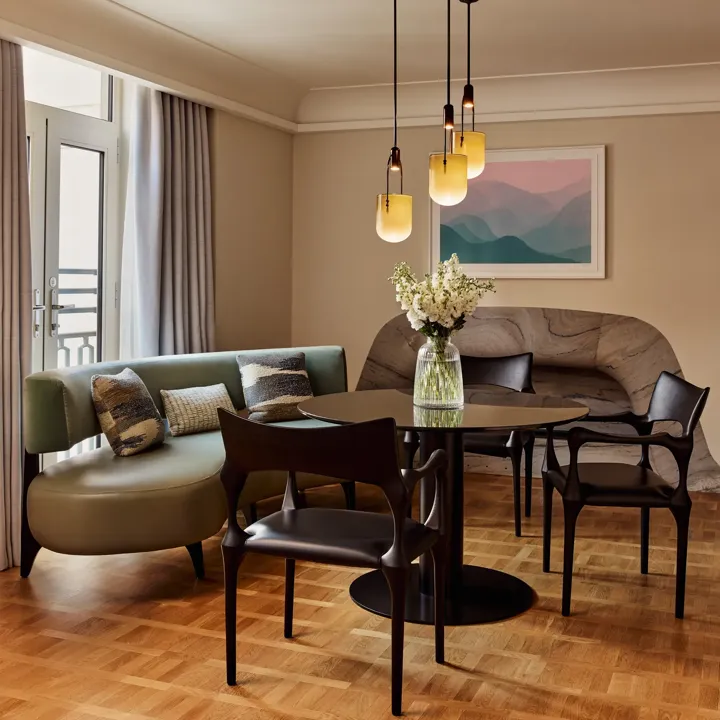 A closer view of the round dining table, green banquette seating, and decorative cushions, with sunlight streaming in through French doors.