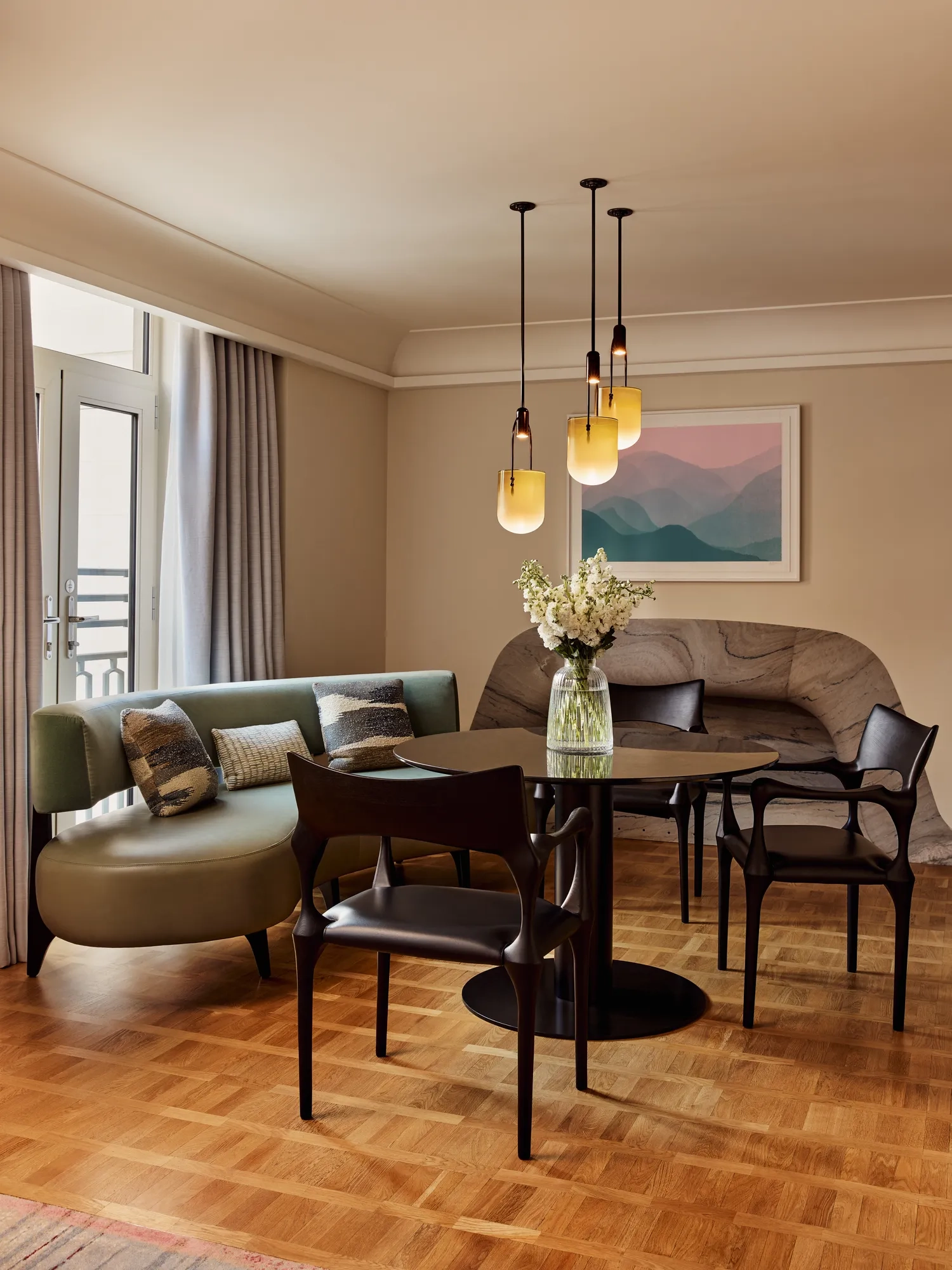 A closer view of the round dining table, green banquette seating, and decorative cushions, with sunlight streaming in through French doors.