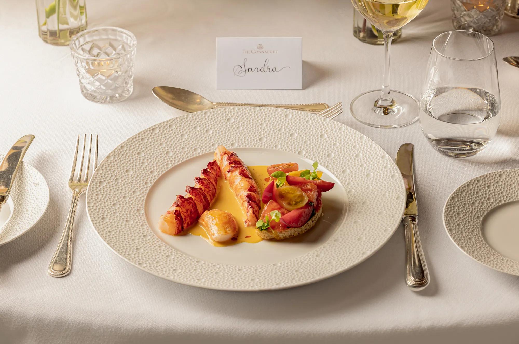 Plated lobster dish with sauce and tomato garnish on an elegantly set dining table.