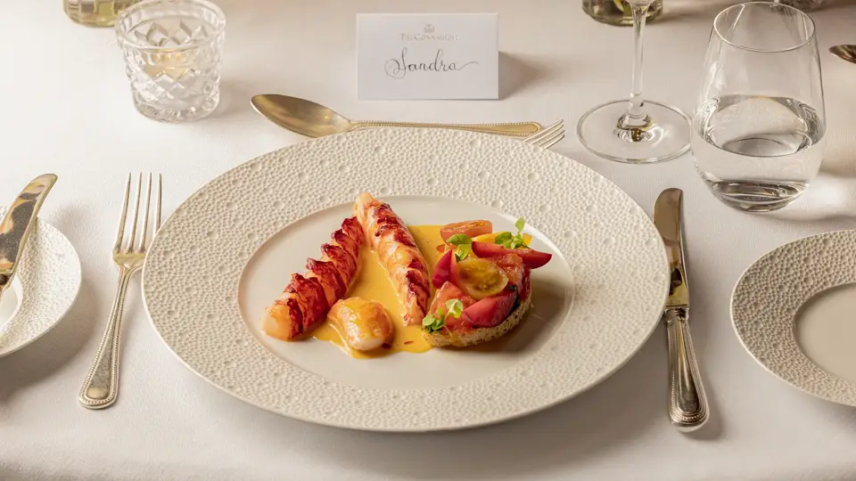 Plated lobster dish with sauce and tomato garnish on an elegantly set dining table.