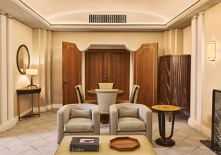 Elegant suite living area with two armchairs, coffee table, round dining table, wood-panelled doors and warm lighting.