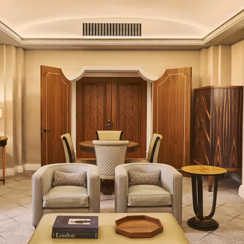 Elegant suite living area with two armchairs, coffee table, round dining table, wood-panelled doors and warm lighting.