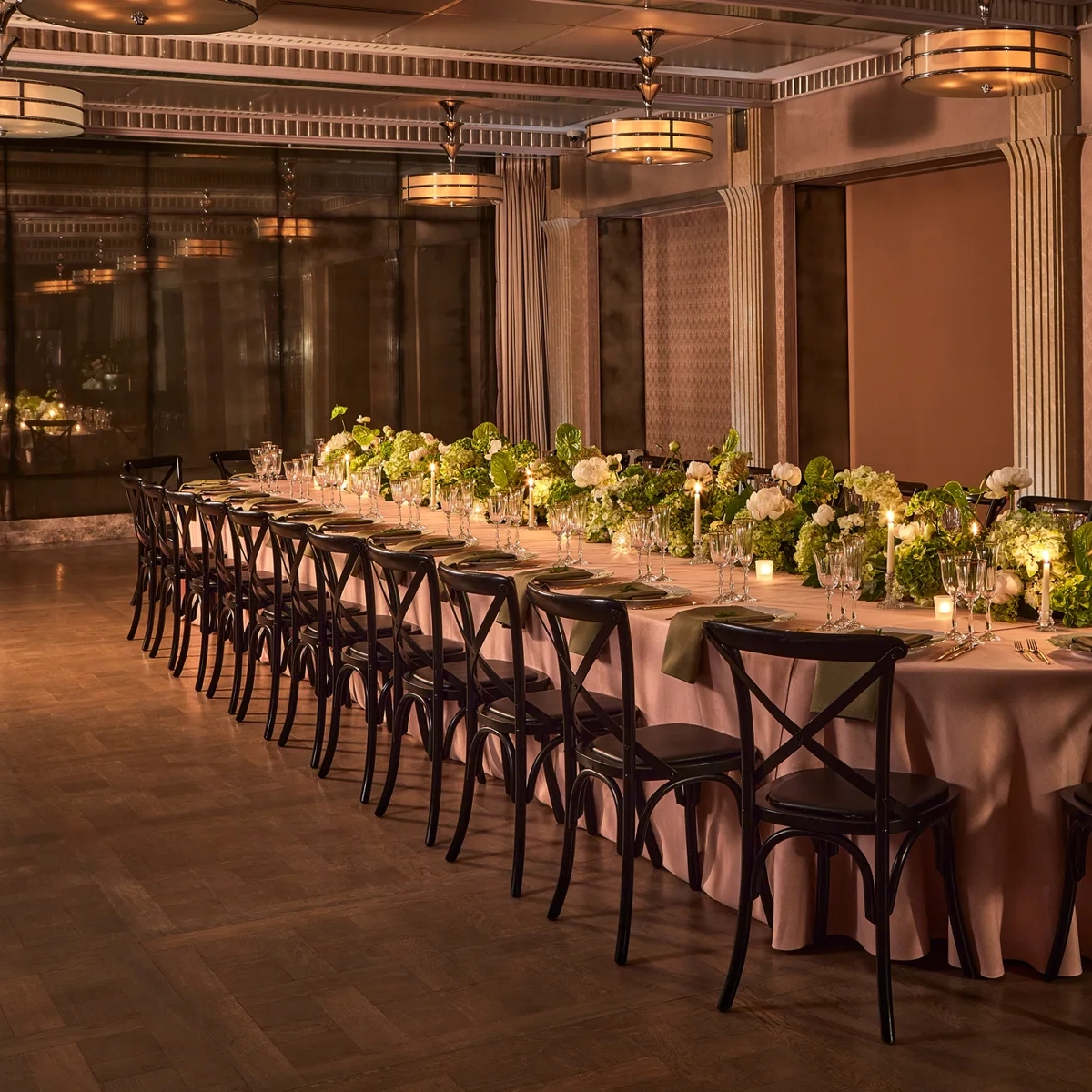 Long banquet table with black chairs, green and white floral arrangements, and candlelight in an elegant dining room.