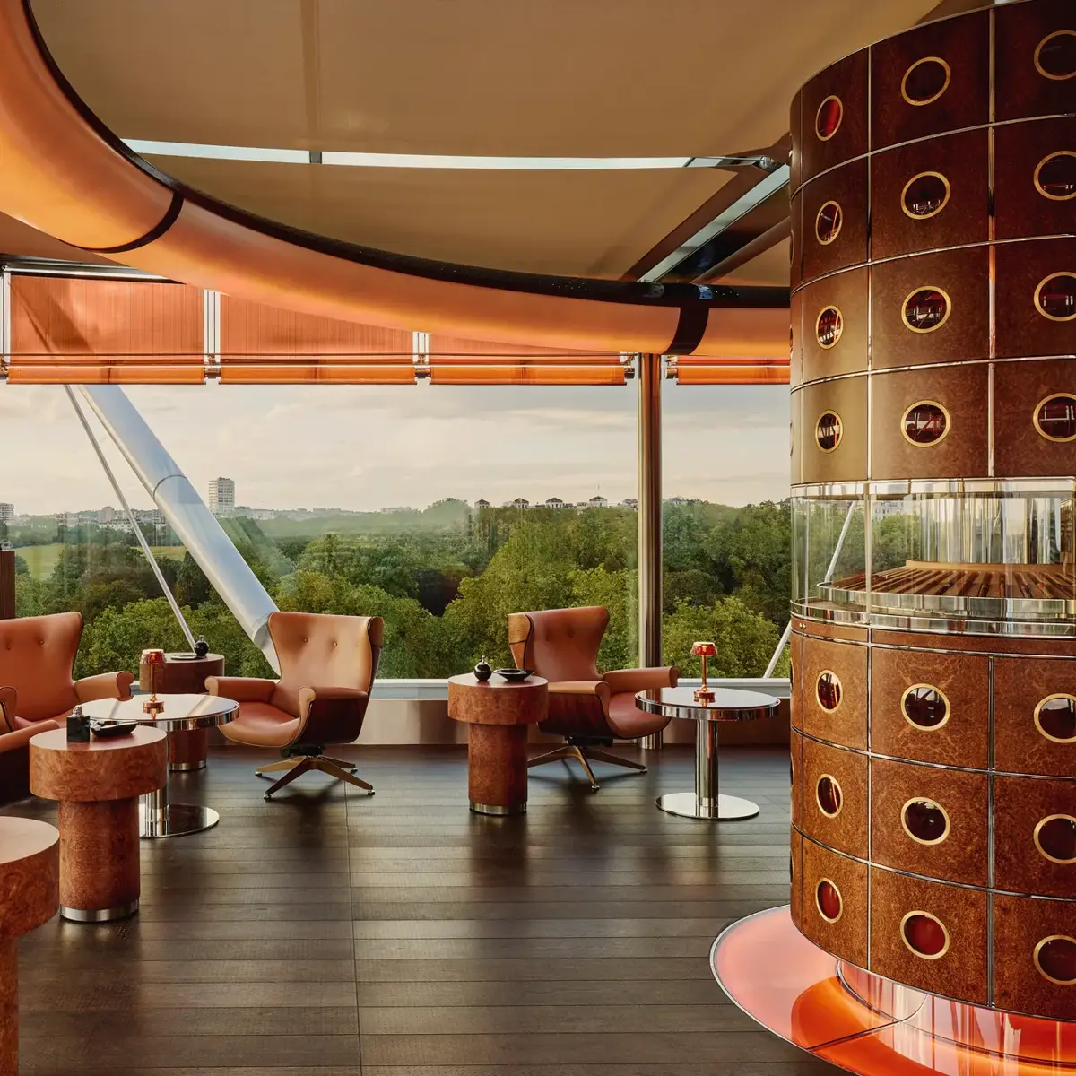 Cigar lounge with caramel leather chairs, circular tables, and a round humidor overlooking Hyde Park through floor-to-ceiling windows.