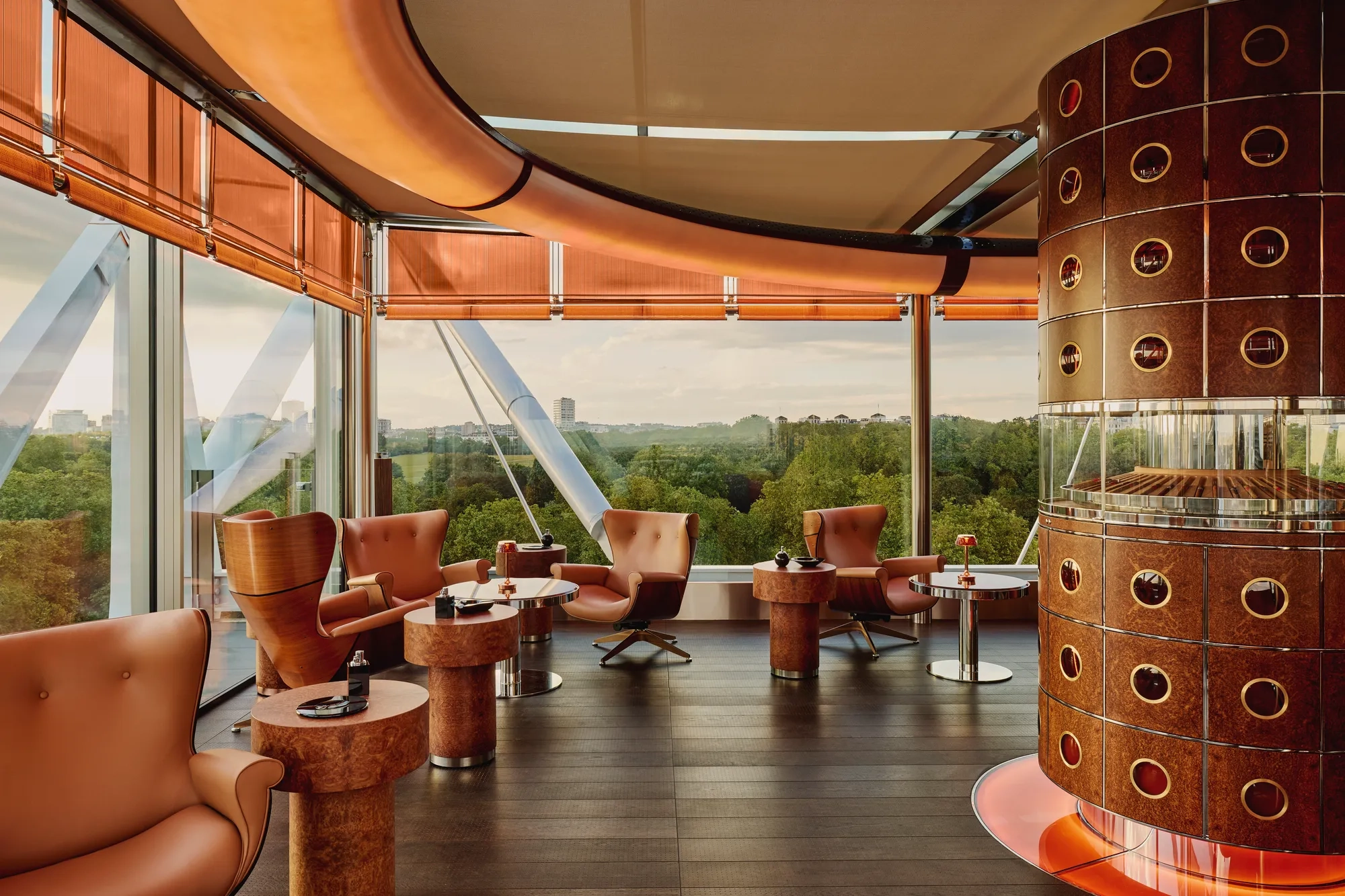 Cigar lounge with caramel leather chairs, circular tables, and a round humidor overlooking Hyde Park through floor-to-ceiling windows.
