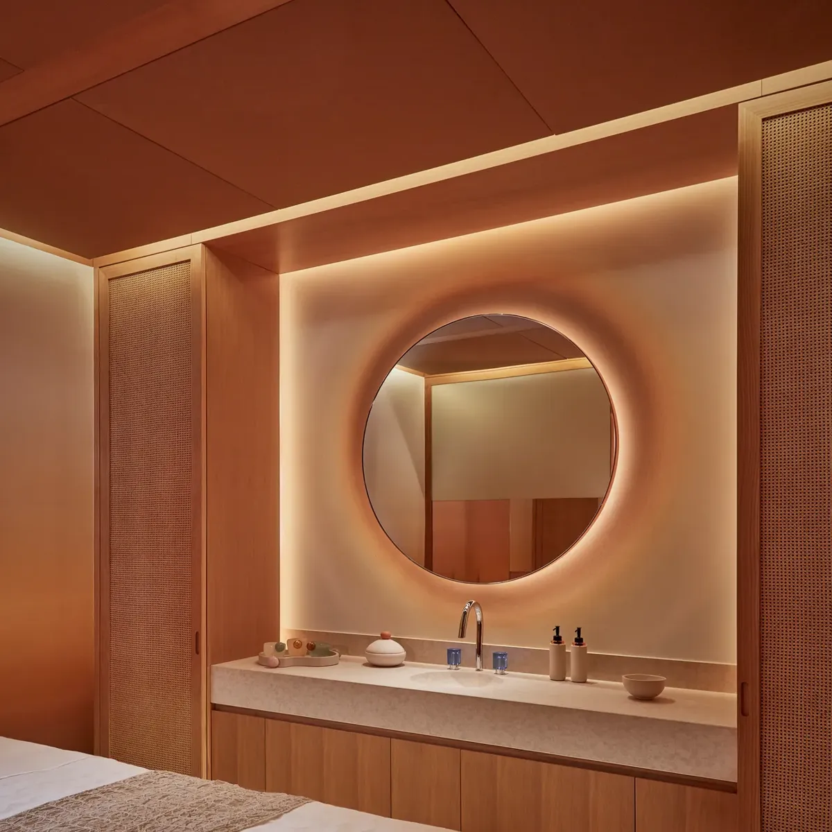 Warmly lit spa treatment room with massage table, round mirror, and natural wood cabinetry for a relaxing experience.