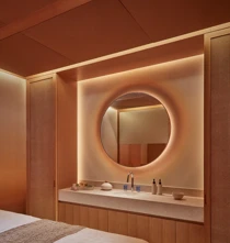 Warmly lit spa treatment room with massage table, round mirror, and natural wood cabinetry for a relaxing experience.