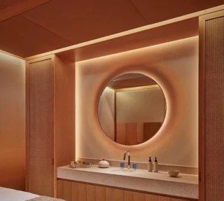 Warmly lit spa treatment room with massage table, round mirror, and natural wood cabinetry for a relaxing experience.