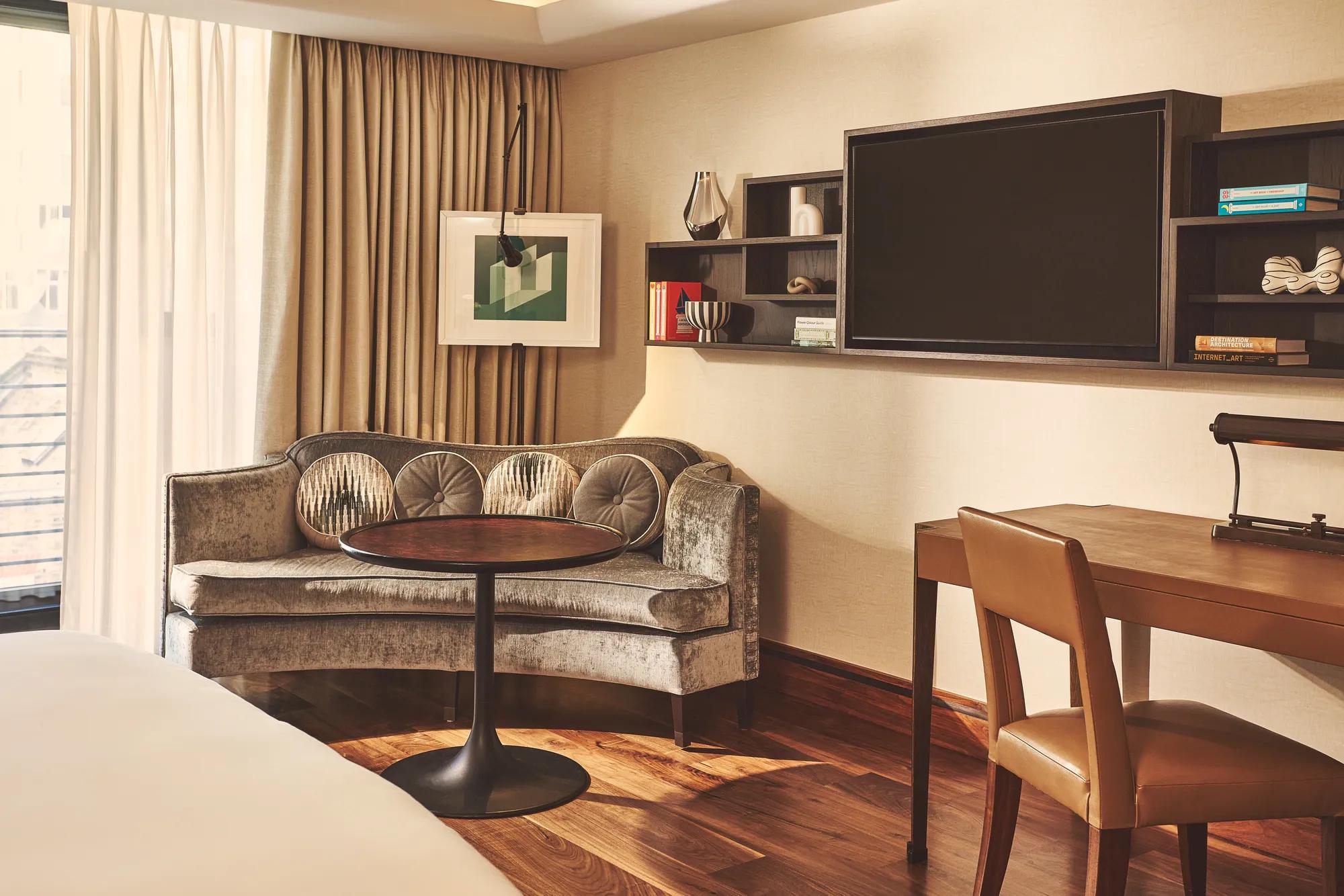 Cozy room corner with a curved sofa, round table, wall-mounted shelves, and large TV beside floor-to-ceiling curtains.